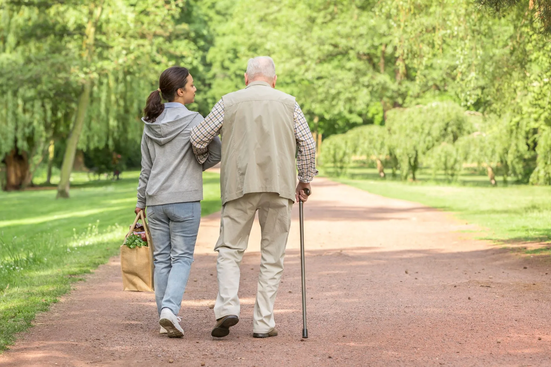 Eine Helferin begleitet einen älteren Mann beim Spaziergang im Park